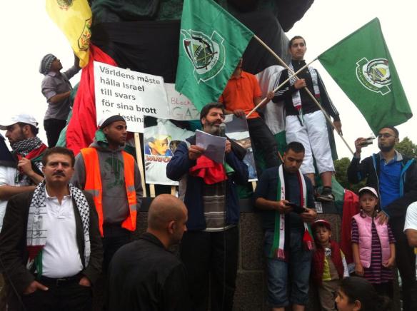 En till synes obekymrad riksdagsledamot, Jamal El-Haj står under terrororganisationen Hamas flagga på PRC:s demonstration på Möllevången sommaren 2014 